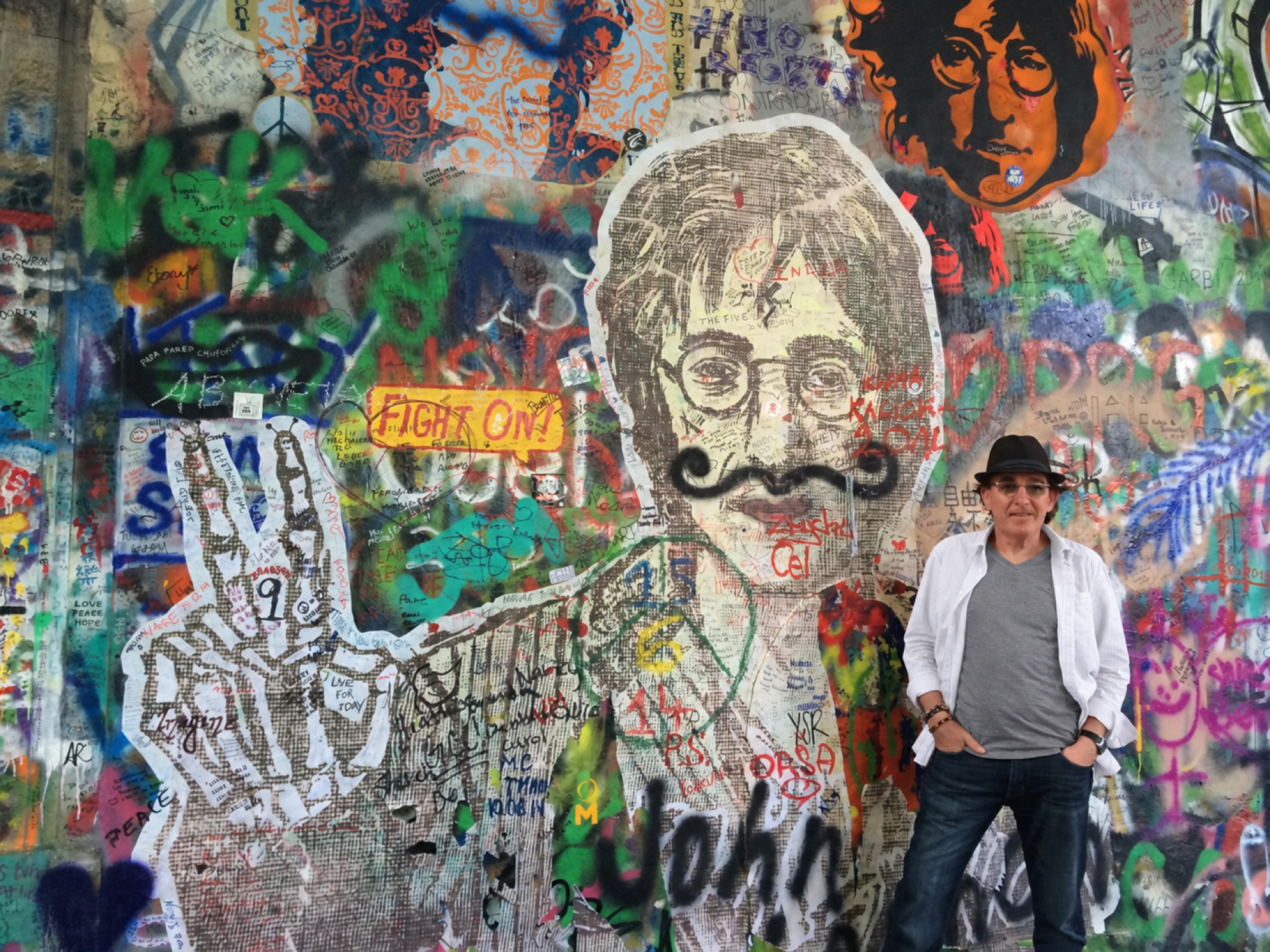Bert in a white overshirt and black hat beside a colourful art-covered wall in Prague